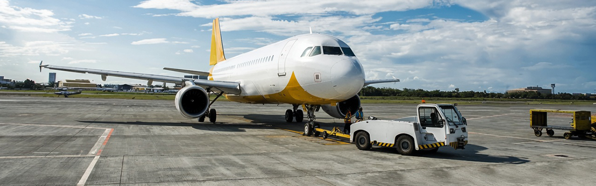 A commercial airplane parked on an airport tarmac with ground support equipment (GSE) nearby, including a tow tractor and service cart.